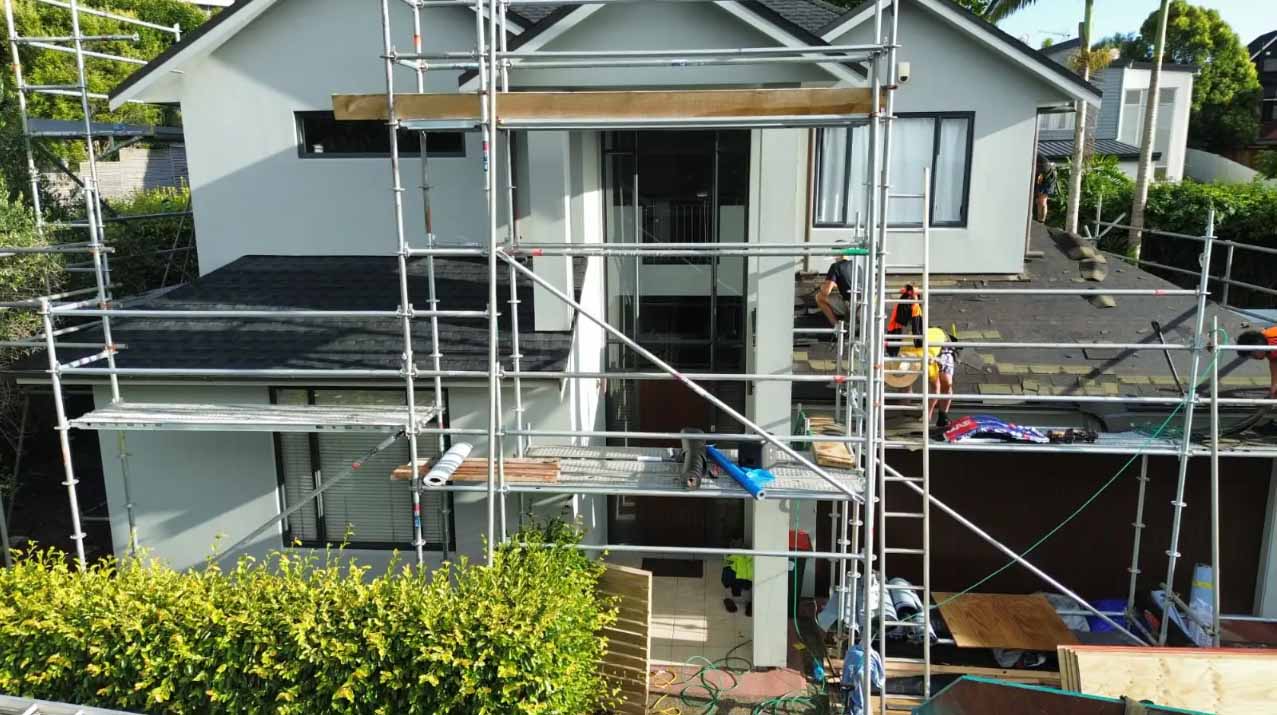 New Zealand home under construction with scaffolding and partially installed asphalt shingle roofing